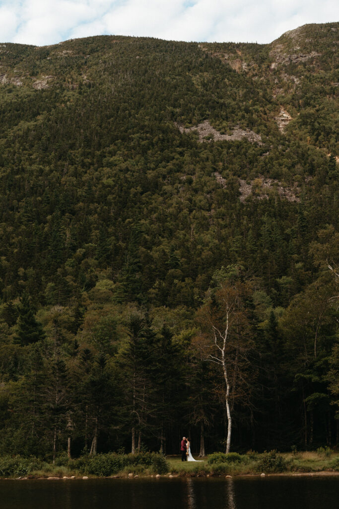 A couple across a lake with a mountain behind them in Crawford Notch.