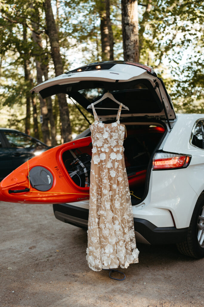 A dress hanging from a car with a kayak behind it during a White Mountain elopement.