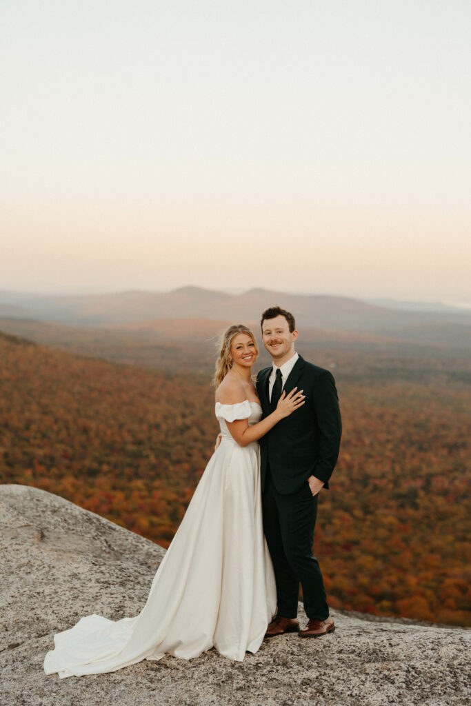 A couple looking at the camera with the fall foliage of Crawford Notch behind them 