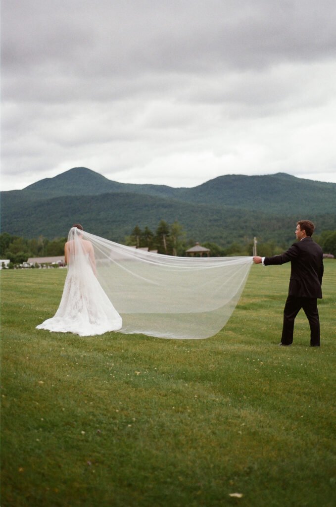 The groom holding the brides cathedral veil with the mountains behind them. 