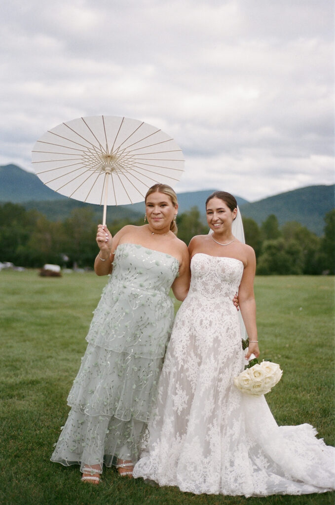 The bride and her sister looking at the camera holding a parasol.