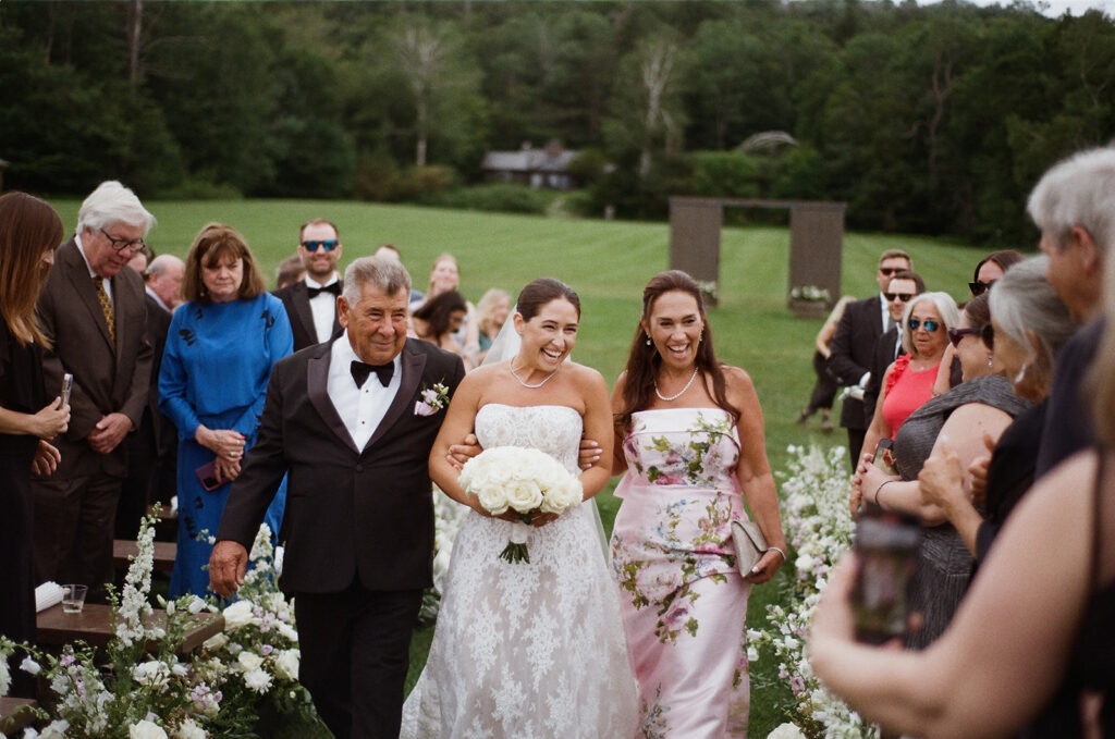 The bride and her parents walking down the aisle laughing. 