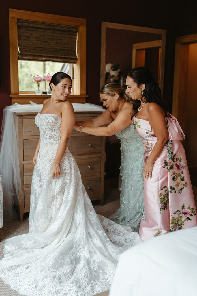 The brides mom and sister helping her zip her wedding dress. 