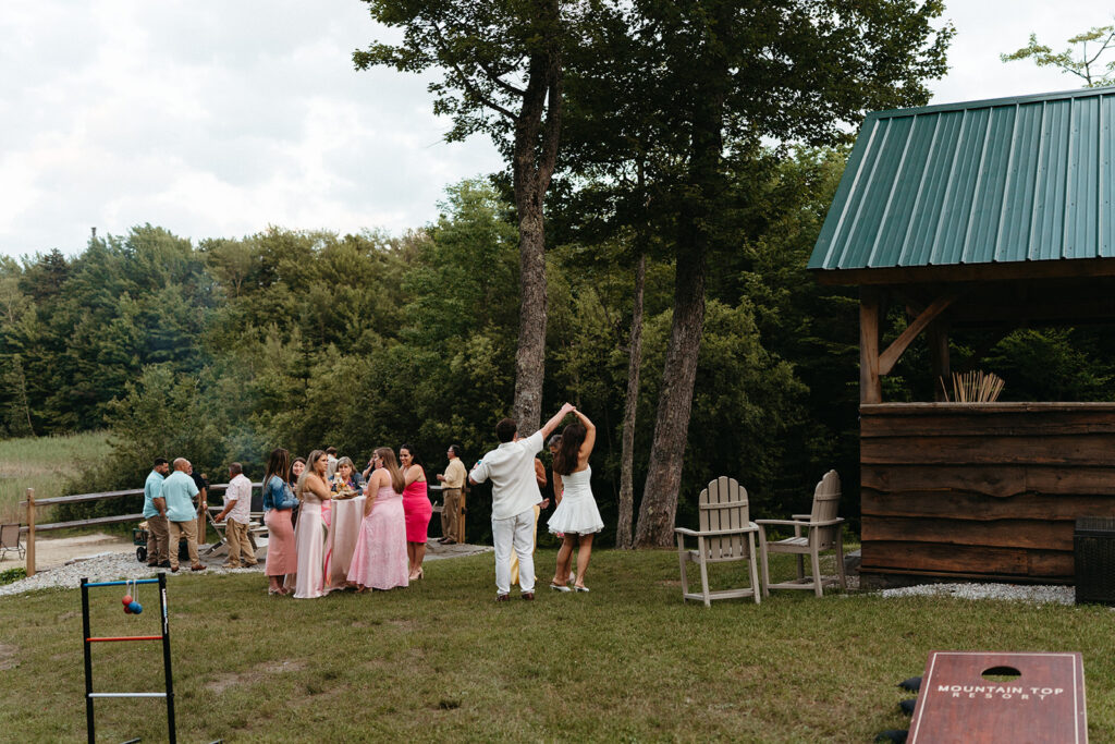 The couple twirling on a lawn with tall trees behind them. 