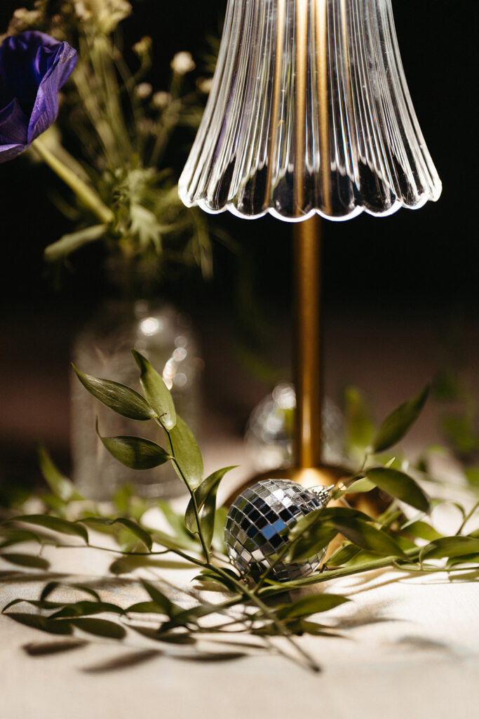 A close up of a small disco ball and lamp with greenery on a cocktail table. 