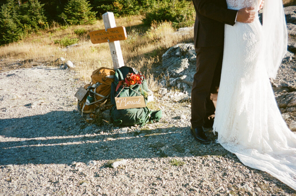 The couple's lower halves and their backpacks leaning again a sign on Mount Mansfield. 