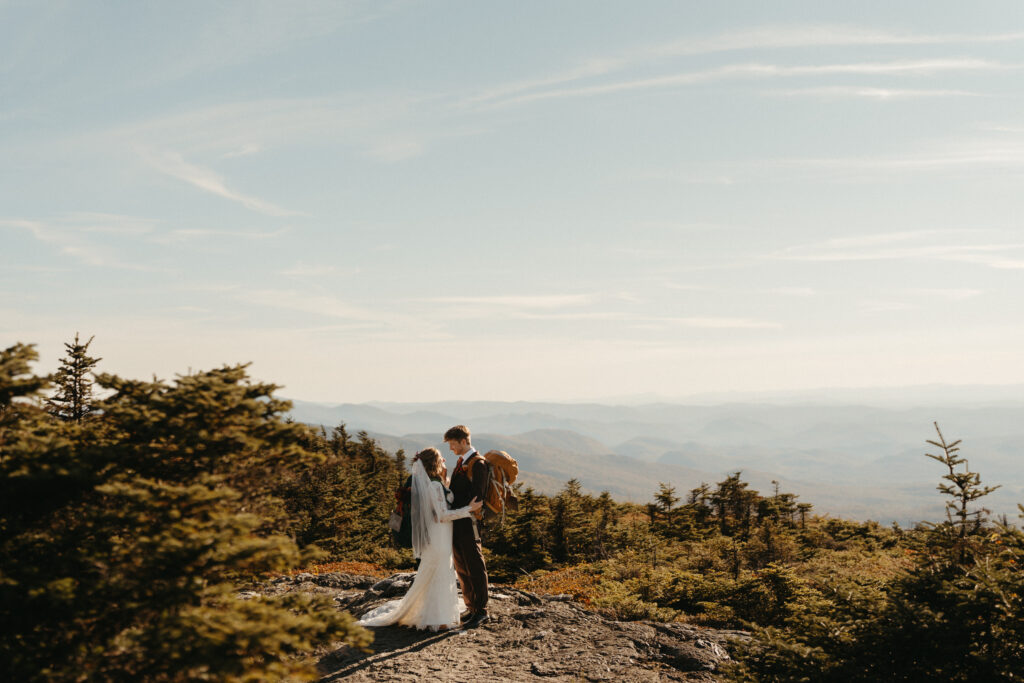 The couple with their backpacks on embracing on Mount Mansfield. 
